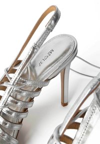 Sandali argento con tacco alto, caratterizzati da molteplici cinturini incrociati, una punta affusolata e una finitura metallica lucida. Presentano una soletta beige.