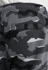 Svart- och gråmönstrade joggingsbyxor med en bakficka och resårmidja. Tyget ser mjukt och texturerat ut.