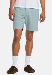 Light blue shorts made of a soft fabric, featuring a straight cut, waistband with a front pocket, paired with white socks and brown slippers.
