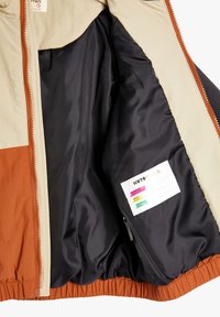 Lichtgewicht jack met een oranje, beige en zwarte kleurenschema. Heeft een gladde binnenvoering en een verzorgingslabel dat aan de binnenkant is genaaid.