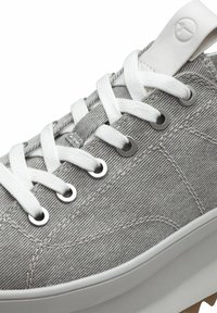 Sneaker in tela grigia con lacci bianchi, occhielli circolari in argento e suola in gomma bianca. Presenta un motivo in tessuto testurizzato e un'etichetta con il logo.
