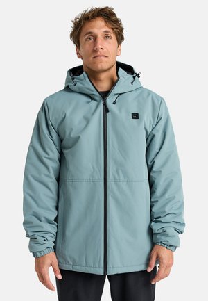 Chaqueta impermeable de color azul claro con capucha, cremallera frontal, puños elásticos y un pequeño logo negro en el pecho. Textura suave, diseño casual.