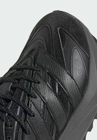 Czarny but sportowy wykonany z mieszanych materiałów z teksturowanymi akcentami, o zaokrąglonym kształcie i sznurowadłach z tkaniny zapewniających pewne dopasowanie.