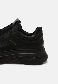 Svart lädersneaker med en kraftig sula, texturerade mönster och diskreta varumärkesdetaljer. Snördesign med vadderad krage för komfort.