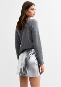 Maglione grigio in lana con una vestibilità rilassata e scollatura rotonda, abbinato a una mini gonna metallica argento lucido con cerniera sul retro.