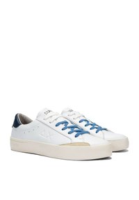 White leather sneakers with blue laces and a navy heel accent. Features a beige suede toe cap and embossed logo on the side. Flat sole.