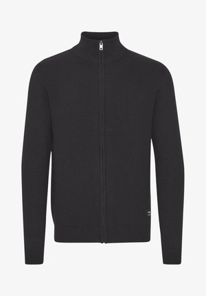 Cárdigan negro con cremallera hecho de tela de punto. Presenta un cuello alto, dobladillo y puños acanalados, y una pequeña etiqueta de marca en el lado inferior.