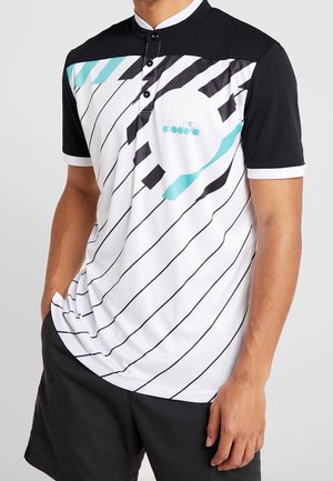 Mann trägt weißes Sportshirt mit kurzen Ärmeln, schwarzen diagonalen Streifen, schwarzen Schultern, türkisfarbenen Akzenten und schwarze Shorts.