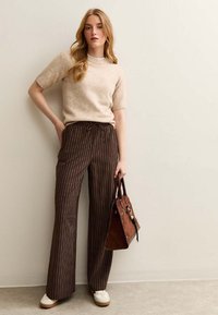 Beige short-sleeve sweater, brown striped wide-leg pants with drawstring. Brown handbag with metal accents, white sneakers. Plain background.