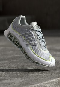 Adidas tekače čevlje s kombinacijo bež in sivo mrežasto zgornjico, neon rumenimi detajli, šestimi podložnimi odprtinami in sivimi vezalkami.