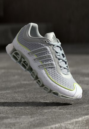 Adidas løbesko med en hvid og grå mesh-overdel, neongule detaljer, seks ventilationslignende stødpods og grå snørebånd.