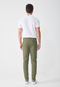 Weißes Poloshirt mit kurzen Ärmeln, grüne Hose mit elastischem Bund und weiße Sneakers mit blauen und roten Akzenten.