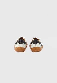 Chaussures en cuir avec un corps principalement crème, des accents noirs et des semelles en caoutchouc marron ; présentent une texture lisse et une forme arrondie.