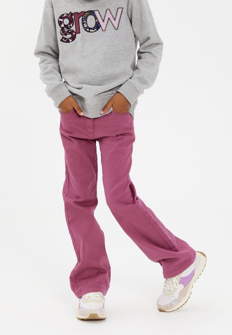 Pantalons en coton violet à coupe décontractée, assortis à un sweat-shirt gris avec un lettrage multicolore "grow" ; baskets blanches et violettes.