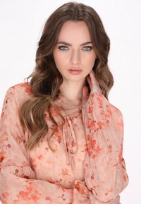 Lichtgewicht, perzikkleurige blouse met bloemmotief. Heeft luchtige mouwen, een striknek en subtiele textuur met verticale strepen.