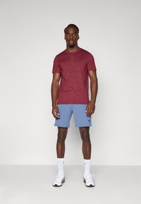 Bordeaux t-shirt met een subtiel patroon, gecombineerd met lichtblauwe shorts. Kenmerken zijn een ronde halslijn en logo-accenten. Eenvoudig sportief ontwerp.