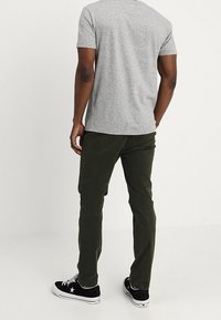 Pantalones oscuros verdes para hombre, de algodón, con un diseño ajustado, textura suave y bolsillos laterales, combinados con una camiseta gris y zapatillas.