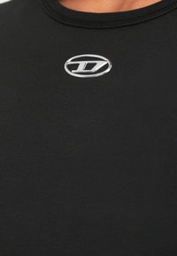 Melnas īsroku krekls no gludas auduma ar izcelto sudraba logo krūšu rajonā, apaļu kakla izgriezumu un smalkām šuvju detaļām.