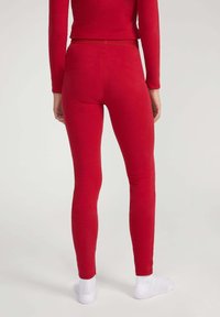 Rode leggings met een slanke pasvorm, gemaakt van zachte stof. De taille is elastisch en het ontwerp heeft geen zichtbare naden. Draagt met witte sokken.