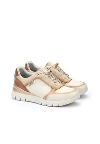 Zapatillas beige y marrón claro con acentos de cuero texturizado, punta redondeada y suela acolchada. Presenta cordones elásticos y materiales contrastantes.