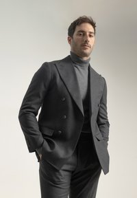 Saco de traje de doble botonadura en gris oscuro, combinado con un cuello alto a juego. Corte ajustado, textura de lana suave y detalles de costura sutiles.