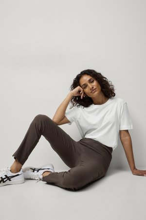 T-shirt bianco di cotone abbinato a pantaloni elasticizzati marroni e sneakers bianche con accenti neri. Modello seduto, che mostra un outfit casual.