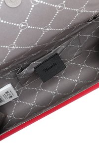 Interior de bolso rojo con forro gris estampado, pequeño bolsillo interior y etiqueta negra de la marca que dice "Tommy Hilfiger".