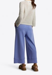 Roomwit gebreide trui met een ronde hals en lange mouwen, gecombineerd met lavendelkleurige broek met wijde pijpen, achterzakken en een gladde textuur.