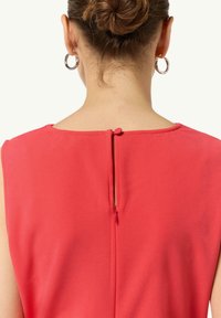 Bezramionowa koralowa sukienka z okrągłym dekoltem. Tył z małym otworem w kształcie klucza z guzikiem jako akcentem. Gładka faktura tkaniny.