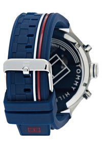 Blå silikon klokkerem med røde og hvite striper, sølvmetallspenne, rund marineblå urskive med hvitt logo og timemarkører.
