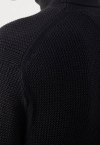 Schwarzer Strickpullover mit strukturiertem Muster, gerippten Akzenten an den Schultern und hohem Kragen. Nahaufnahme des Rückendesigns.