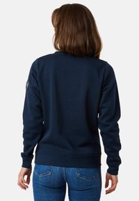 Marineblauwe crewneck sweatshirt met ribgebreide manchetten en zoom. Zachte stof en een rond logo-embleem op de linkermouw. Klassiek pasvormontwerp.