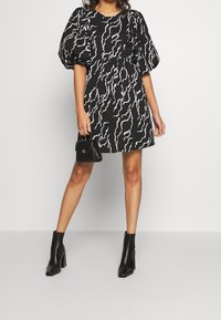 Svart klänning med vitt abstrakt mönster, puffärmar, åtsittande midja och A-linjeformad kjol. Kombinerad med svarta ankelboots och en liten handväska.