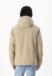 Beige waterdichte jas met een capuchon, gekenmerkt door een gladde textuur en een ontspannen pasvorm. De achterkant toont een naadloos ontwerp en geen zichtbare bevestigingsmiddelen.