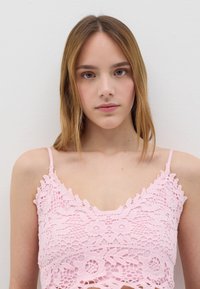 Top corto in pizzo rosa con intricate fantasie floreali, spalline regolabili e un orlo a scalloped. Materiale leggero e testurizzato.