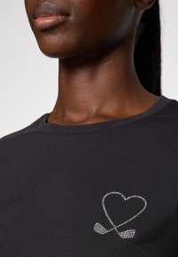 Zwarte t-shirt met korte mouwen, voorzien van een zilveren rhinestone hart en gekruiste peddels op de linkerborst. Zachte stof.