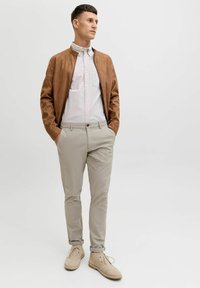 Brązowa skórzana bomberka na jasnoniebieską koszulę z guzikami, w połączeniu z beżowymi chinosami i jasnobrązowymi sznurowanymi butami. Prosty design, luźny krój.