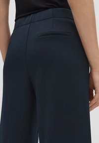 Pantalons ajustés bleu marine avec une texture lisse, présentant une poche arrière discrète et une silhouette à jambe large.