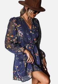Marineblauw bloemenrok met doorschijnende lange mouwen, diepe V-halslijn en een cinched taille. Heeft kleurrijke bloem motieven en een ontspannen pasvorm.