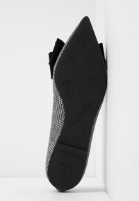 Chaussure plate à bout pointu avec motif pied-de-poule noir et blanc, détail nœud noir, et semelle embossée de dessins de chaussons de ballet et de la marque.