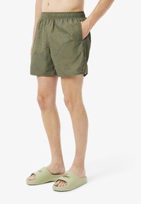 Groene zwemshorts met een topografisch patroon in het blauw, elastische tailleband, twee zijzakken. Gecombineerd met lichtgroene slipper sandalen met logo.