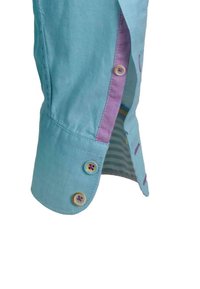 Hellblauer Hemdmanchette mit zwei Knöpfen, lila Innenseite und gestreiftem Stoff, der durch die Öffnung des Ärmels sichtbar ist.