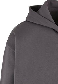 Sudadera gris de tejido suave, con capucha ajustable, cuello acanalado y hombros caídos para un ajuste relajado.