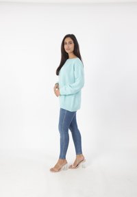 Maglione a collo rotondo di colore blu chiaro, con spalle scese e maniche a costine, abbinato a jeans scuri aderenti e sandali trasparenti con tacco a blocco.