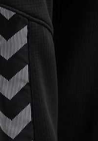 Top atletico nero con una texture a coste. Presenta un motivo a chevron bianco sul lato, che accentua il design delle maniche.