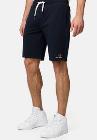 Mørkeblå bomuldsshorts med elastisk talje, hvid snor og sidelommer; har orange logo "Est. 1993" på venstre side.