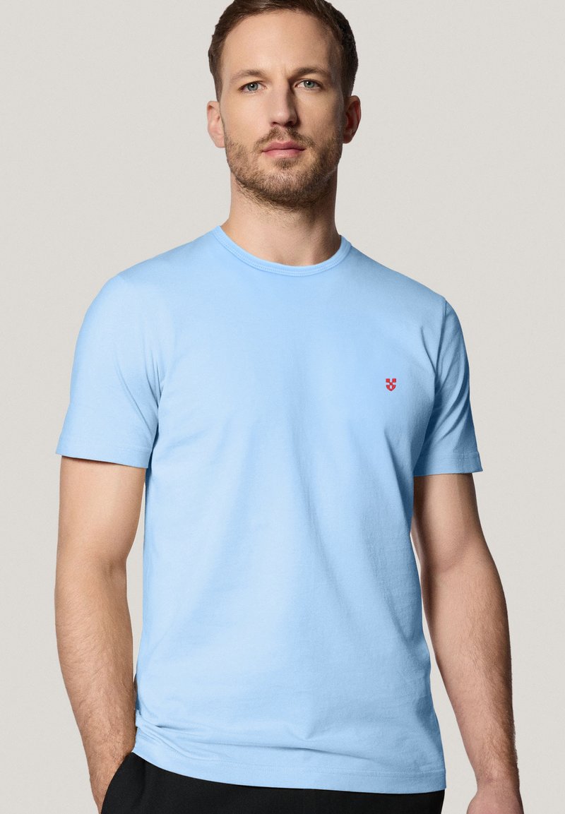 Jasnoniebieska bawełniana koszulka z krótkim rękawem i okrągłym dekoltem, z małym czerwonym emblematem na lewej piersi.