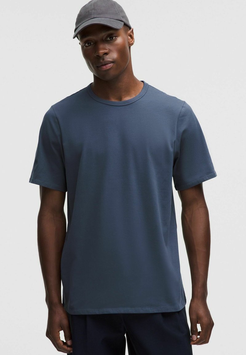 T-shirt en coton bleu marine avec un col rond et des manches courtes. Texture lisse et coupe décontractée, accompagné d'une casquette grise.