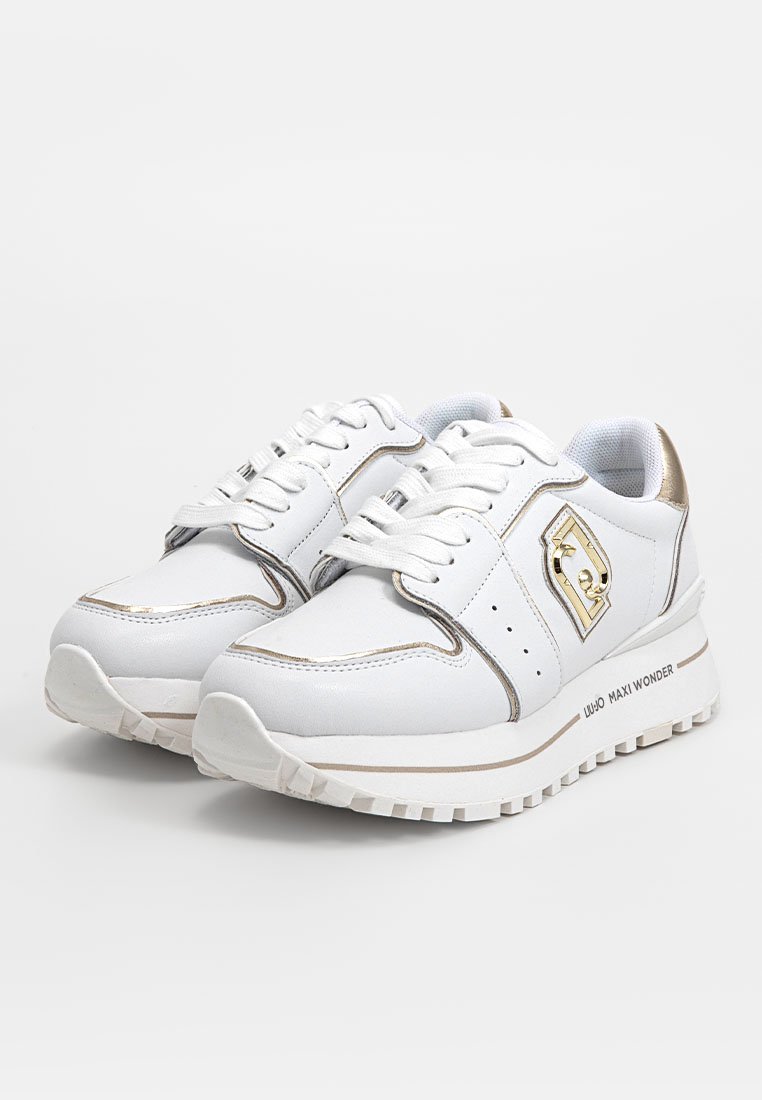 Zapatillas deportivas blancas con acentos dorados, lados texturizados, cierre con cordones y suela gruesa. Cuenta con un detalle del logotipo en el lateral.