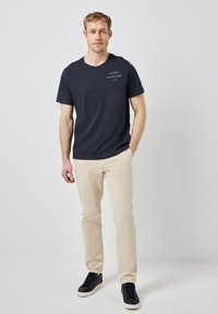 Námořnické modré tričko s krátkým rukávem a kulatým výstřihem, na hrudi s bílým textem, kombinované s béžovými kalhotami a černými teniskami.